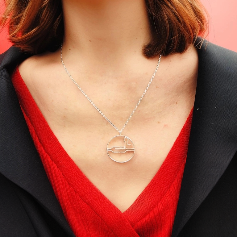 Close-up of a woman wearing the CRISPR necklace, showcasing its elegant design. The circular pendant is prominently displayed against a red V-neck top and a black blazer. Close-up of a woman wearing the CRISPR necklace, showcasing its elegant design. The circular pendant is prominently displayed against a red V-neck top and a black blazer.