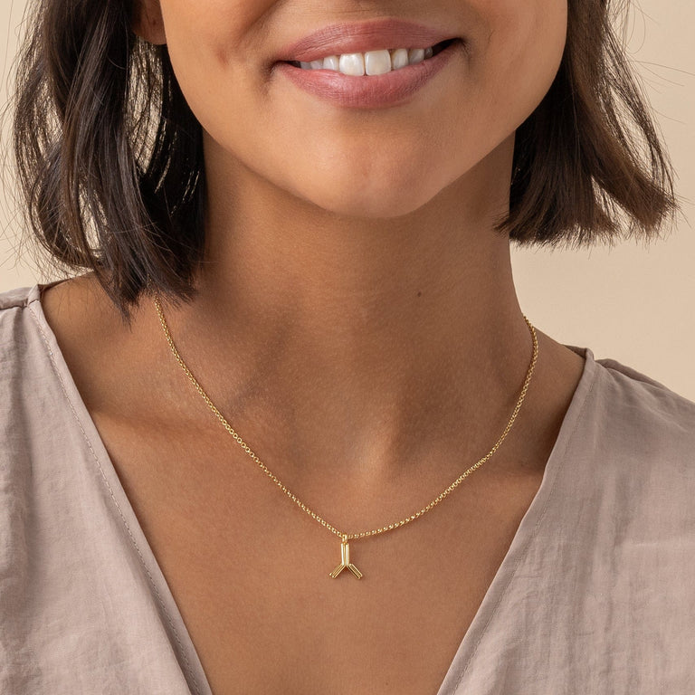 Close-up of gold antibody necklace on model, showcasing scientific design for health enthusiasts. Close-up of gold antibody necklace on model, showcasing scientific design for health enthusiasts.