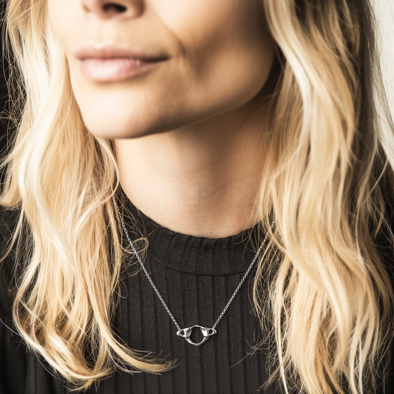 Close-up of a blonde woman wearing a black top and the sterling silver Atlas Necklace, shaped like the vertebra that supports the head. Close-up of a blonde woman wearing a black top and the sterling silver Atlas Necklace, shaped like the vertebra that supports the head.