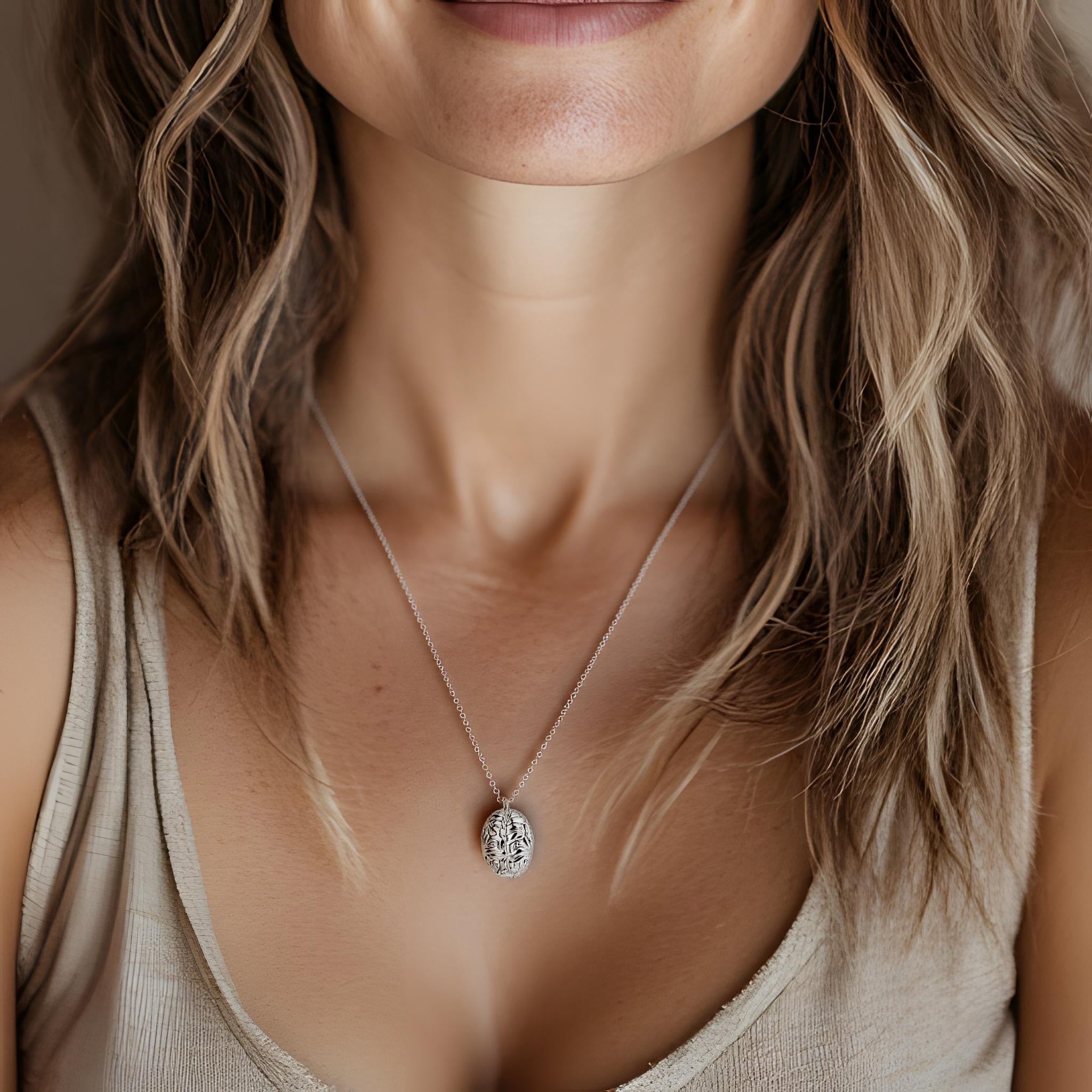 Close-up of a woman wearing a silver brain-inspired pendant necklace on a delicate chain. The necklace features an intricate design resembling a human brain. She is dressed in a beige tank top, and her wavy, light brown hair frames her neck. The background is softly blurred, creating a warm and elegant aesthetic. Close-up of a woman wearing a silver brain-inspired pendant necklace on a delicate chain. The necklace features an intricate design resembling a human brain. She is dressed in a beige tank top, and her wavy, light brown hair frames her neck. The background is softly blurred, creating a warm and elegant aesthetic.