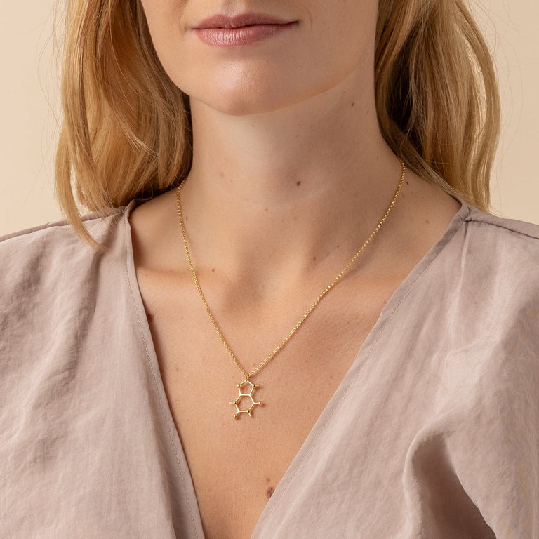 Elegant gold vermeil caffeine necklace on woman – sleek science-inspired design for coffee aficionados. Elegant gold vermeil caffeine necklace on woman – sleek science-inspired design for coffee aficionados.