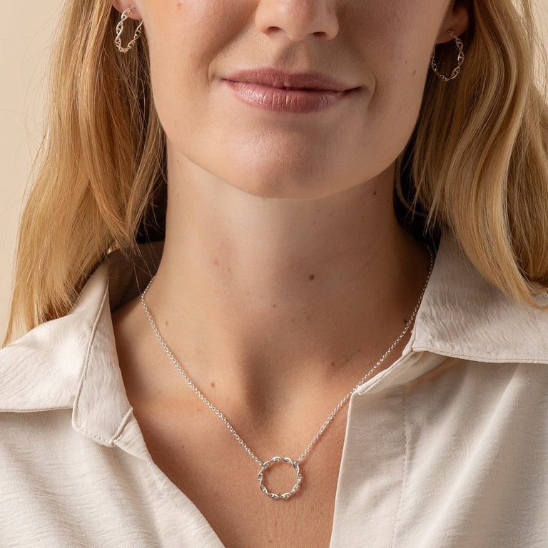 a model wearing the Circular DNA Necklace, highlighting the intricate silver design against a neutral backdrop. a model wearing the Circular DNA Necklace, highlighting the intricate silver design against a neutral backdrop.