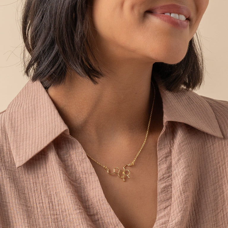 Close-up of dopamine-serotonin necklace in gold vermeil on model, showing fine molecular detail and craftsmanship. Close-up of dopamine-serotonin necklace in gold vermeil on model, showing fine molecular detail and craftsmanship.