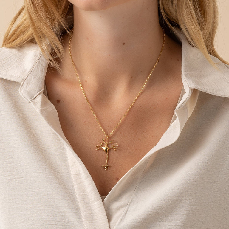 Woman wearing the neuron necklace in gold vermeil, displaying the elegant design on a neckline, perfect for science lovers. Woman wearing the neuron necklace in gold vermeil, displaying the elegant design on a neckline, perfect for science lovers.
