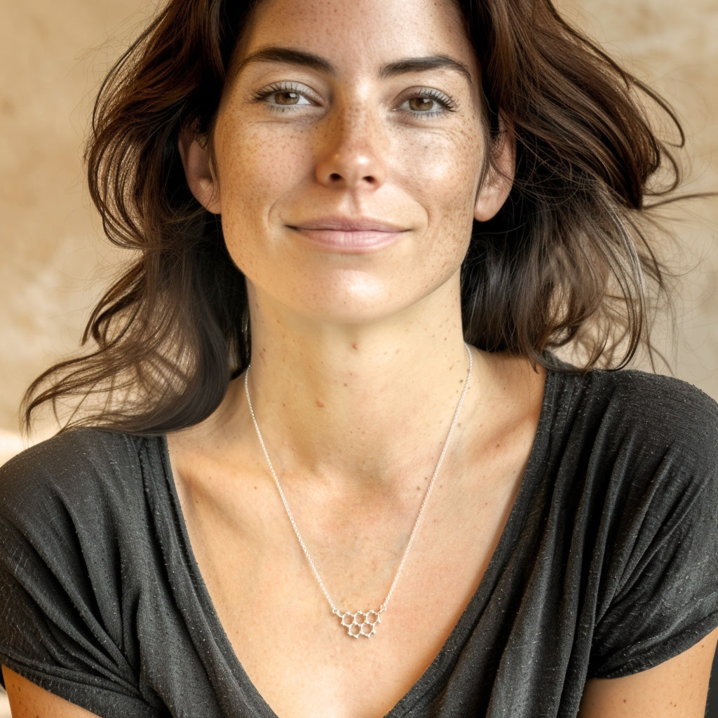 Woman wearing the silver graphite necklace against a dark grey V-neck shirt, smiling softly while showing the necklace clearly. Woman wearing the silver graphite necklace against a dark grey V-neck shirt, smiling softly while showing the necklace clearly.