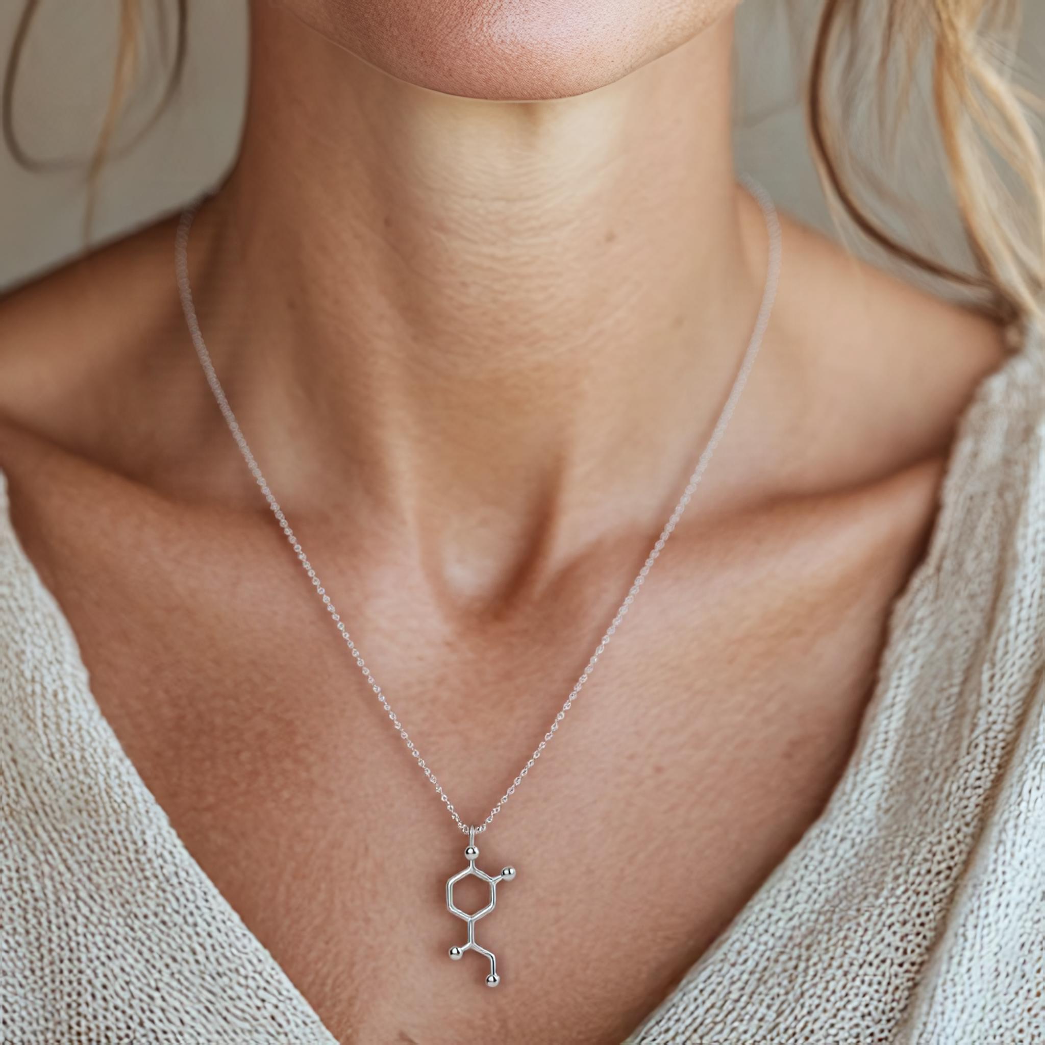 A close-up of a woman wearing the silver noradrenaline necklace, showcasing its elegant molecular design resting against her collarbone. A close-up of a woman wearing the silver noradrenaline necklace, showcasing its elegant molecular design resting against her collarbone.