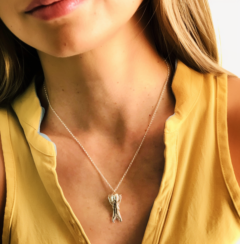 Close-up of a woman wearing the platypus skull necklace. The silver pendant hangs on a fine chain around her neck. She is wearing a yellow blouse, and her long, brown hair is visible. Close-up of a woman wearing the platypus skull necklace. The silver pendant hangs on a fine chain around her neck. She is wearing a yellow blouse, and her long, brown hair is visible.
