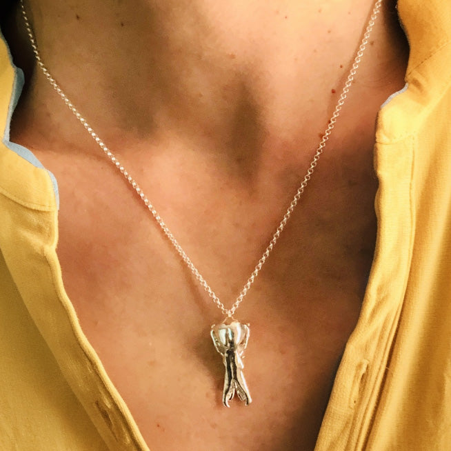 Close-up shot of the platypus skull necklace resting on the collarbone of a woman wearing a yellow top. The silver pendant is detailed and hangs on a thin chain. Close-up shot of the platypus skull necklace resting on the collarbone of a woman wearing a yellow top. The silver pendant is detailed and hangs on a thin chain.