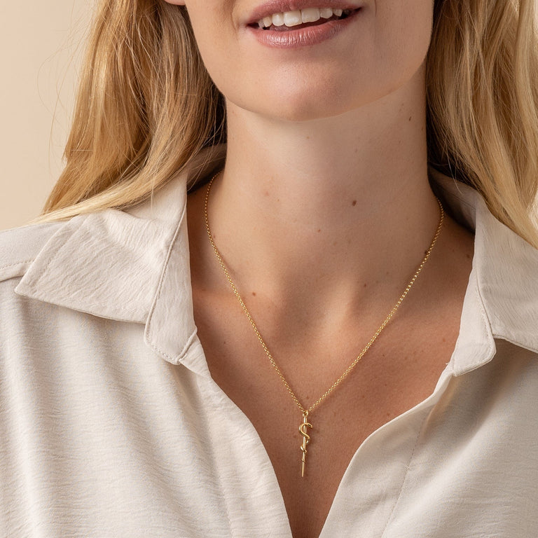 Close-up of the Rod of Asclepius gold vermeil necklace worn by a model, showcasing its elegant and symbolic design. Close-up of the Rod of Asclepius gold vermeil necklace worn by a model, showcasing its elegant and symbolic design.