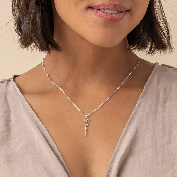 Close-up of the Rod of Asclepius necklace worn by a model, highlighting its elegant and symbolic design for healthcare professionals. Close-up of the Rod of Asclepius necklace worn by a model, highlighting its elegant and symbolic design for healthcare professionals.