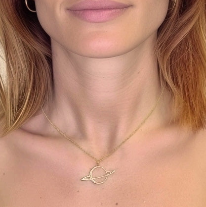 Close-up view of a gold Saturn necklace resting just below the collarbone of a woman with light skin and auburn hair. Close-up view of a gold Saturn necklace resting just below the collarbone of a woman with light skin and auburn hair.