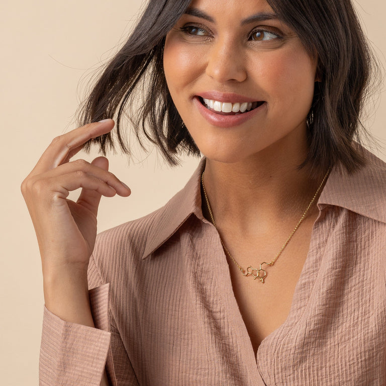 Model gently touching dopamine-serotonin necklace in gold vermeil, highlighting the necklace’s scientific and stylish appeal. Model gently touching dopamine-serotonin necklace in gold vermeil, highlighting the necklace’s scientific and stylish appeal.