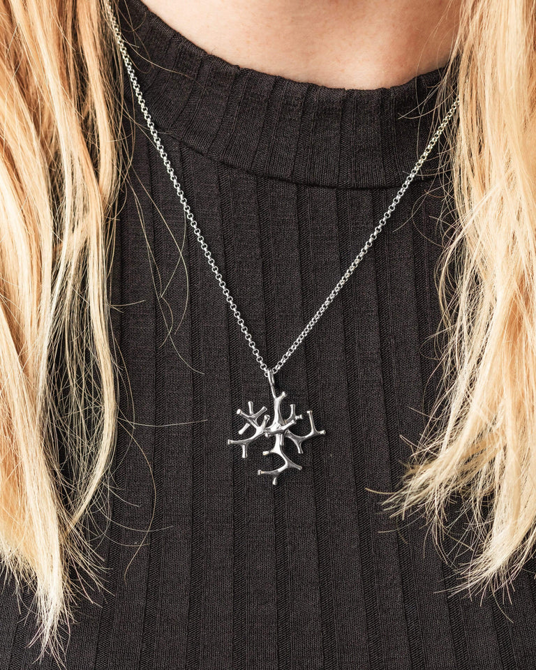 Woman wearing the Astrocyte Necklace in silver, showcasing its detailed star-like design. Woman wearing the Astrocyte Necklace in silver, showcasing its detailed star-like design.