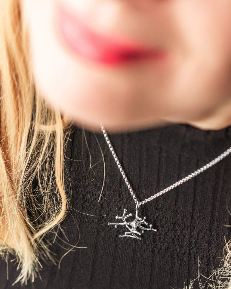 Close-up of a silver astrocyte necklace, featuring intricate cell-inspired craftsmanship. Close-up of a silver astrocyte necklace, featuring intricate cell-inspired craftsmanship.