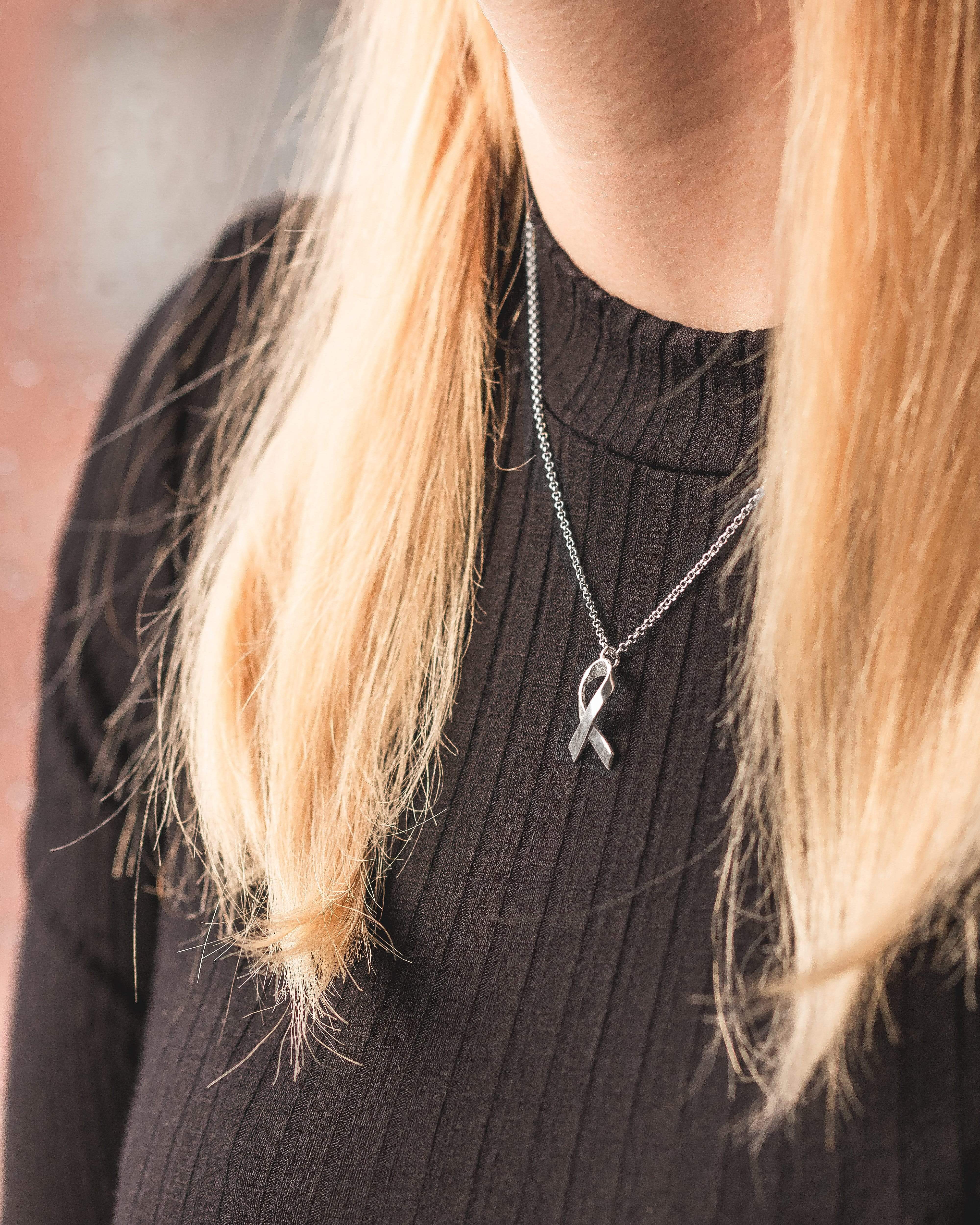 Woman wearing silver awareness ribbon necklace, showcasing elegant design and scientific inspiration. Woman wearing silver awareness ribbon necklace, showcasing elegant design and scientific inspiration.