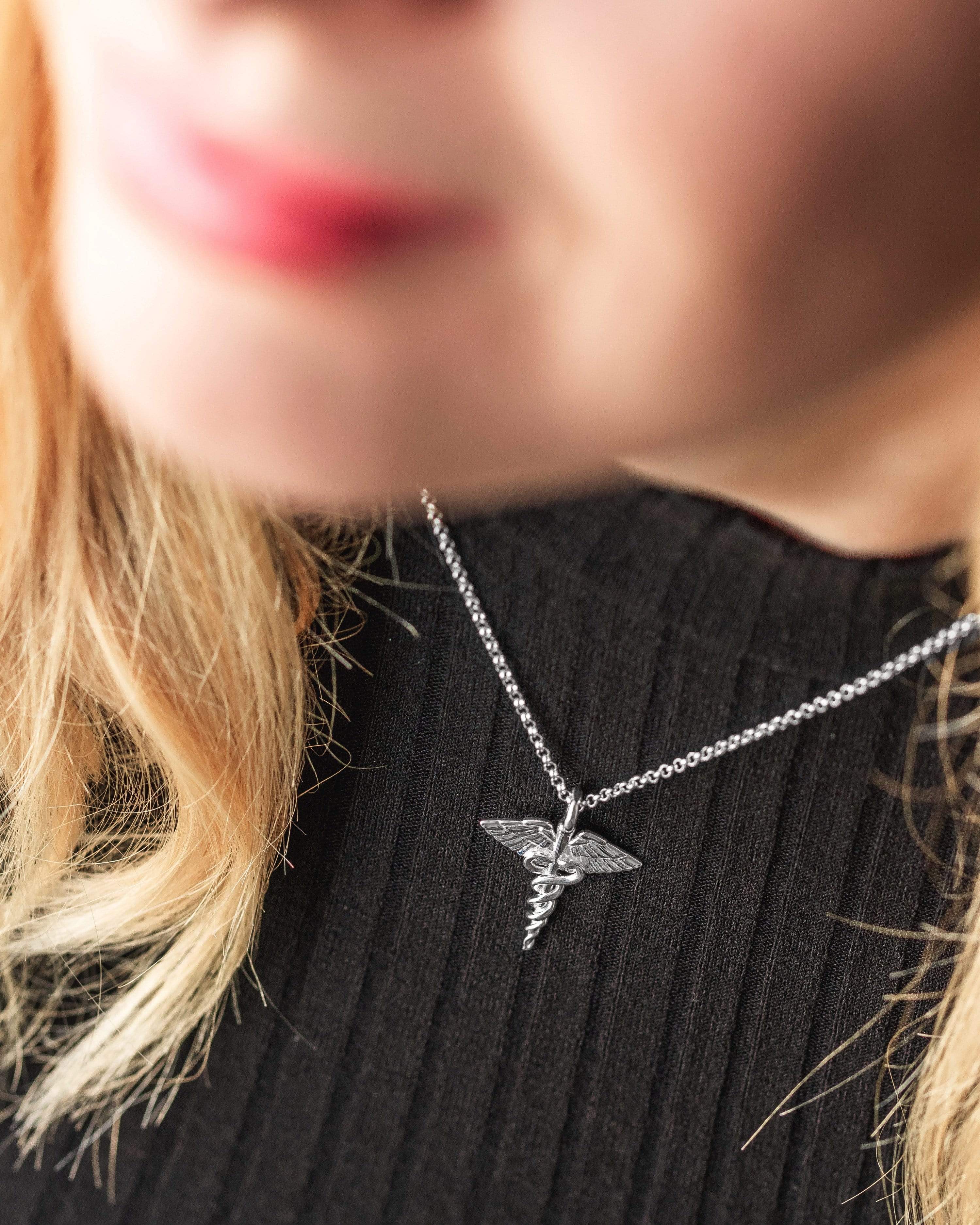A woman wearing the caduceus necklace, showcasing its intricate design and stylish appeal for healthcare professionals. A woman wearing the caduceus necklace, showcasing its intricate design and stylish appeal for healthcare professionals.