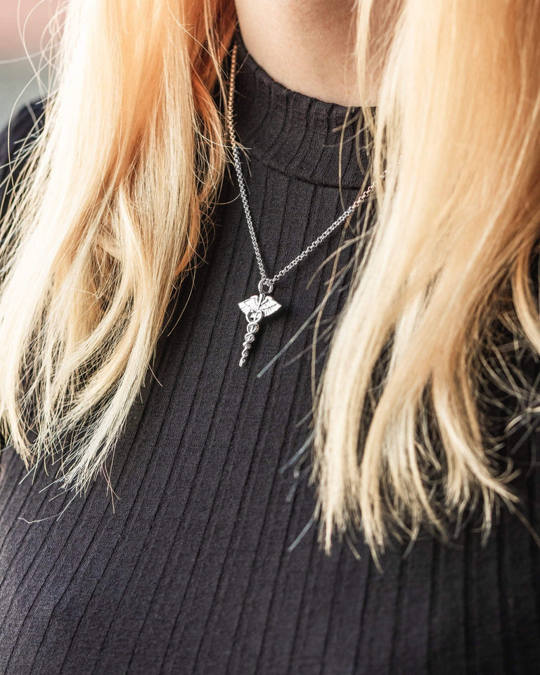 The caduceus necklace styled with a black top, highlighting its elegant silver finish and mythological inspiration. The caduceus necklace styled with a black top, highlighting its elegant silver finish and mythological inspiration.