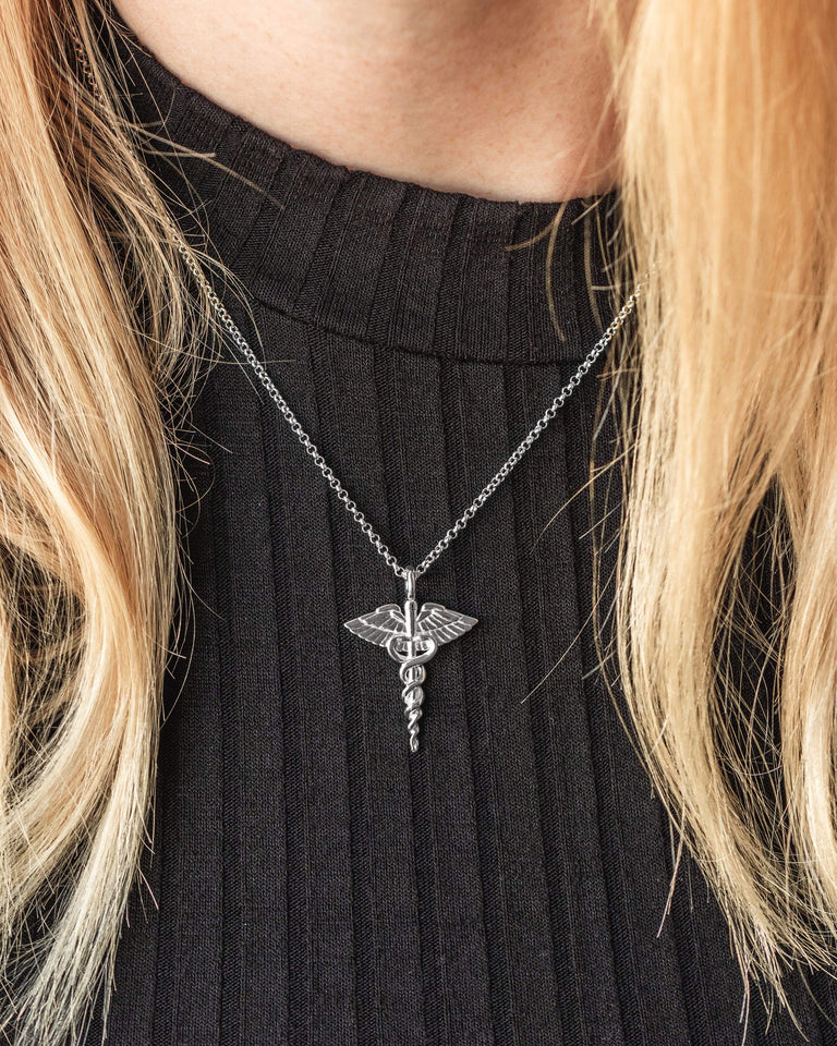 Sterling silver caduceus necklace displayed on a model, emphasizing its delicate craftsmanship and scientific symbolism. Sterling silver caduceus necklace displayed on a model, emphasizing its delicate craftsmanship and scientific symbolism.