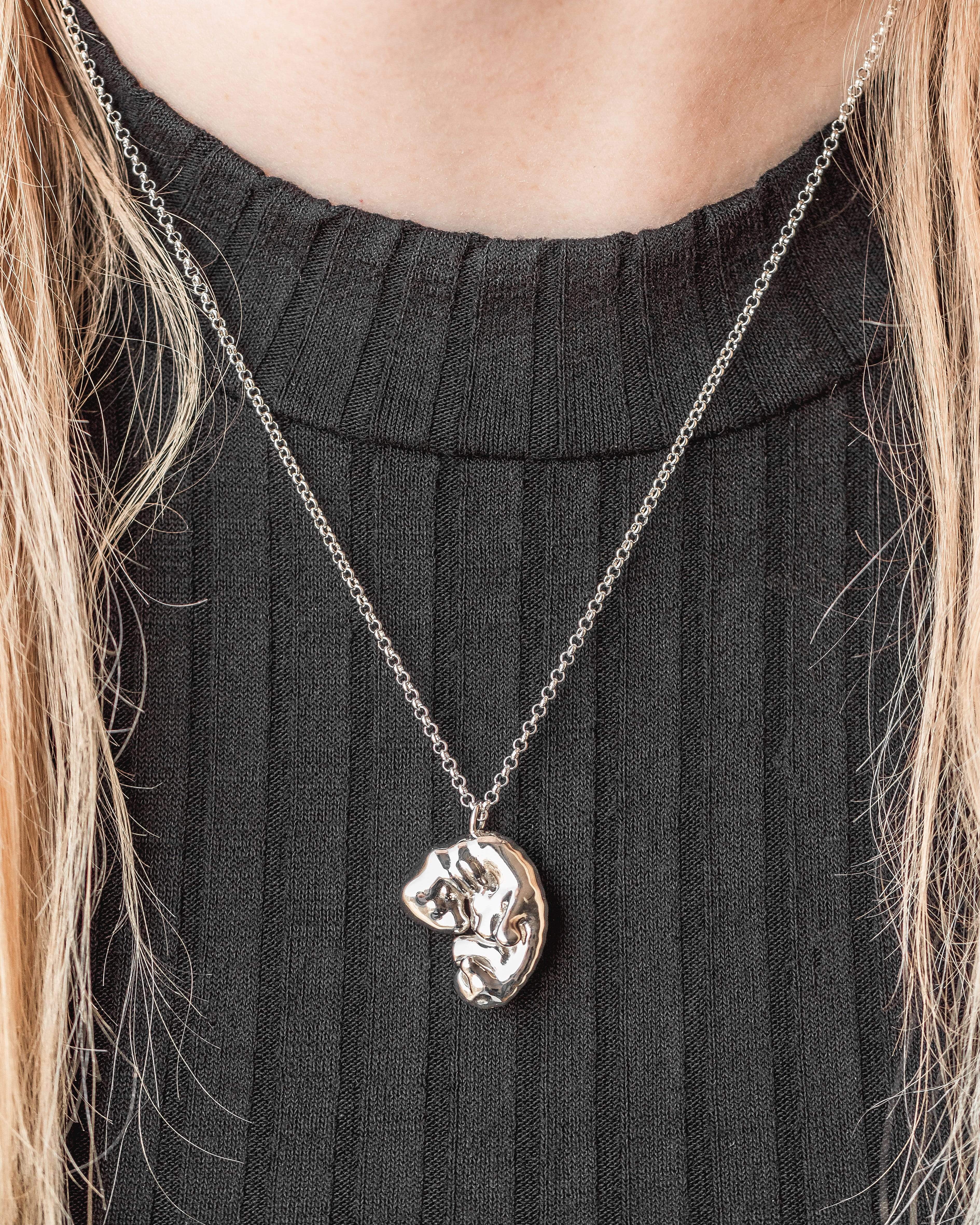 Close-up of the silver embryo necklace worn on a model, showcasing its intricate details. Close-up of the silver embryo necklace worn on a model, showcasing its intricate details.