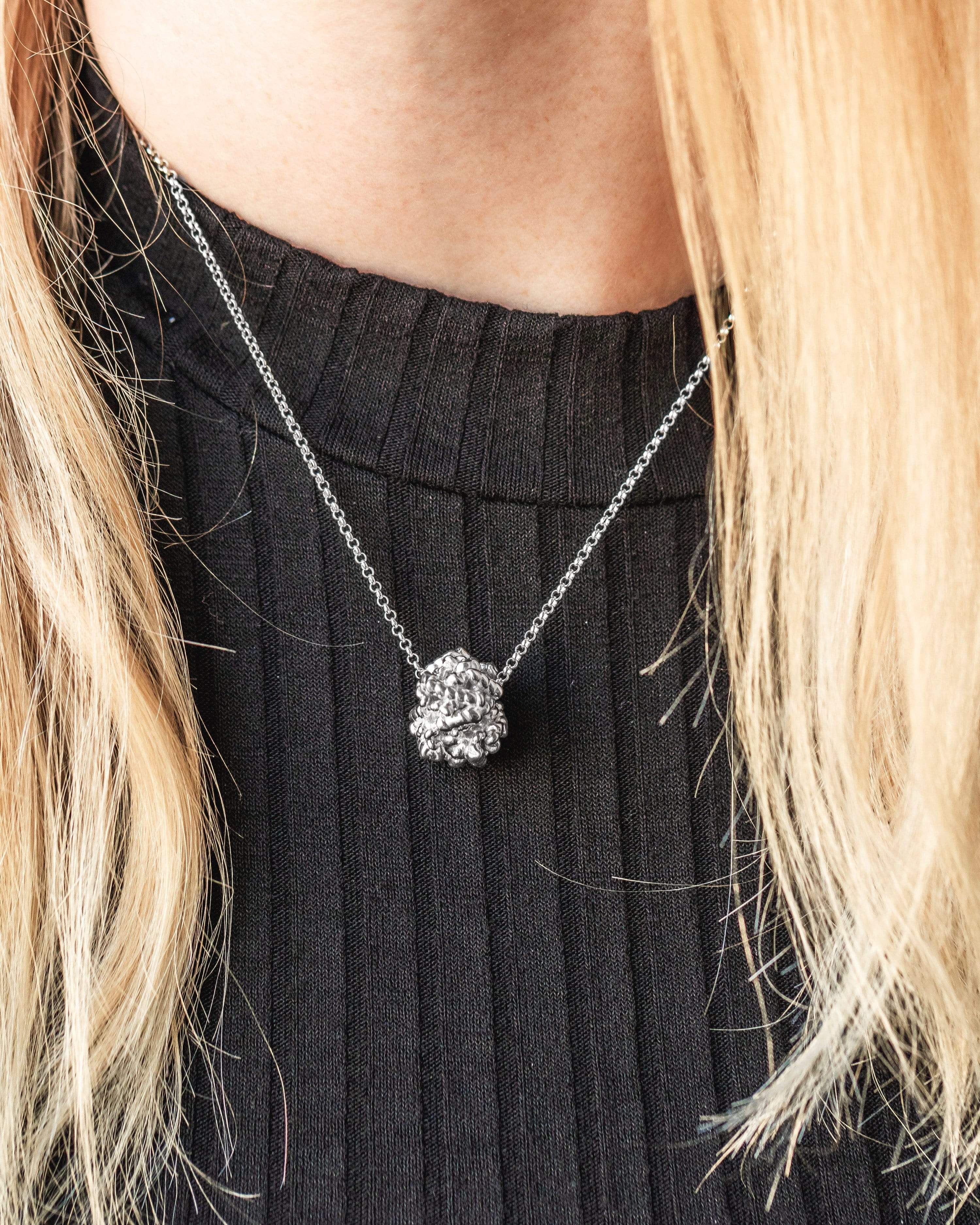 Close-up of a hemoglobin necklace in sterling silver, showing intricate 3D-printed details of the protein structure. Close-up of a hemoglobin necklace in sterling silver, showing intricate 3D-printed details of the protein structure.