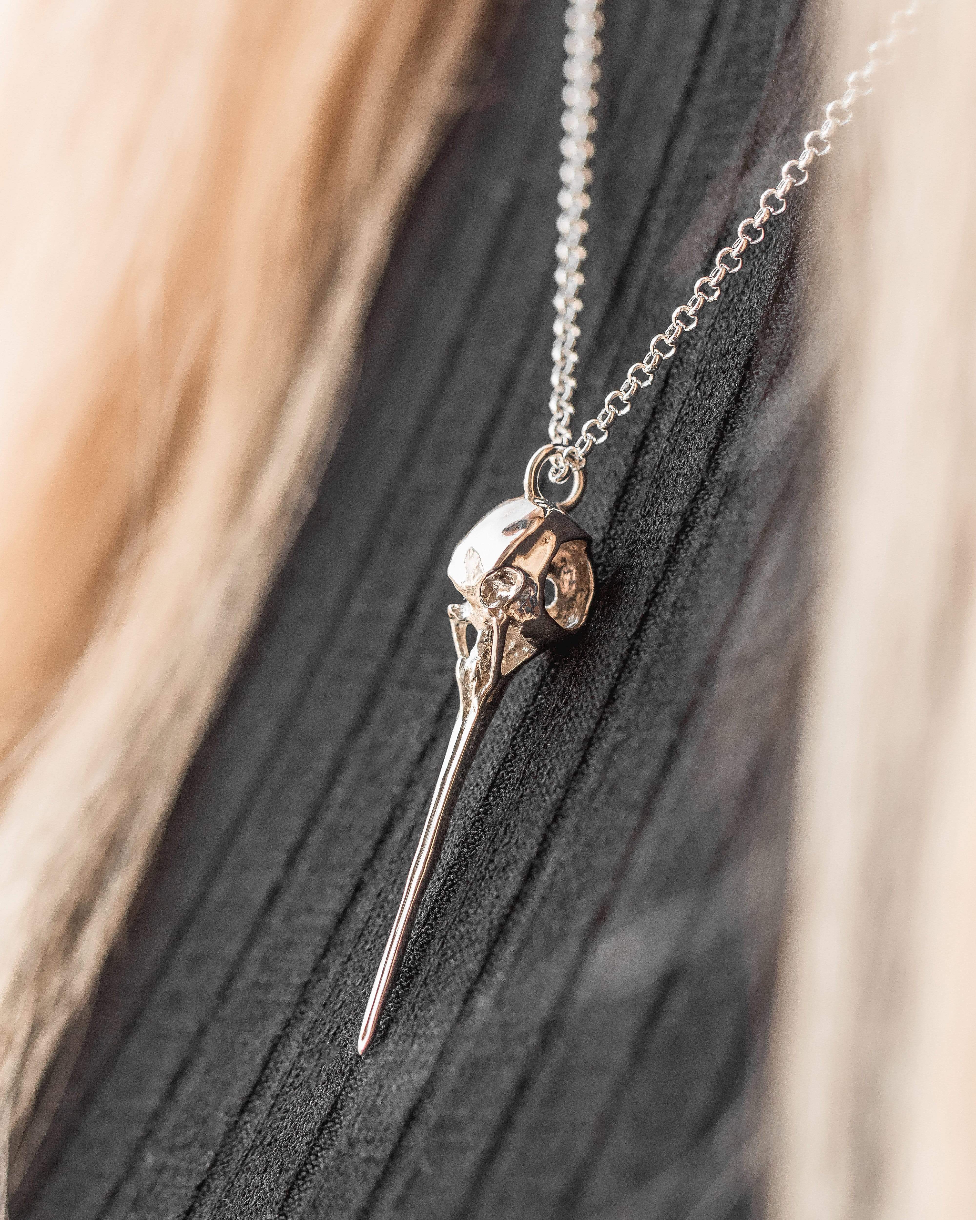 A woman wearing the hummingbird skull necklace, elegantly styled on a black top. A woman wearing the hummingbird skull necklace, elegantly styled on a black top.