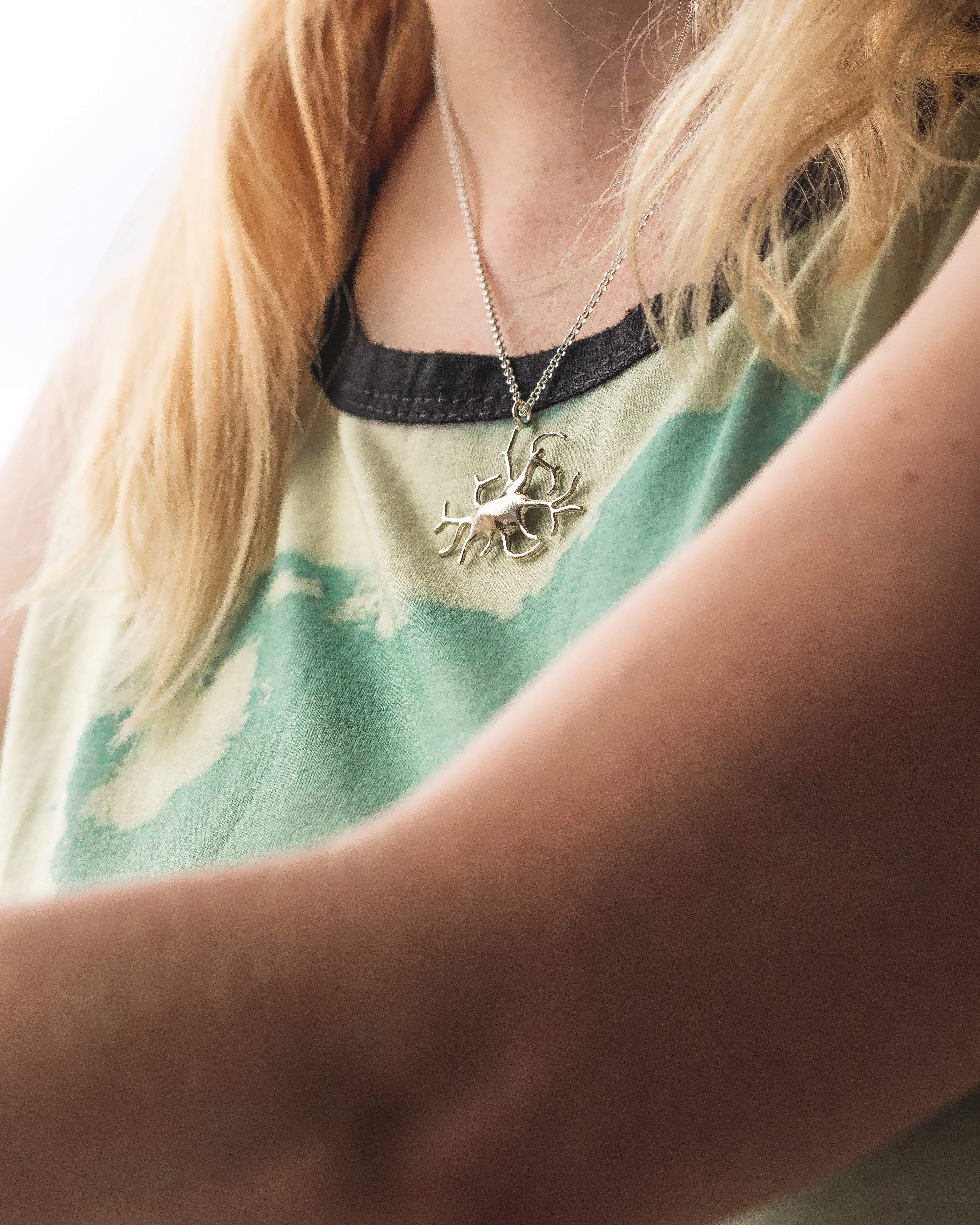 Close-up view of the silver melanocyte necklace, featuring a detailed scientific cell structure. Close-up view of the silver melanocyte necklace, featuring a detailed scientific cell structure.