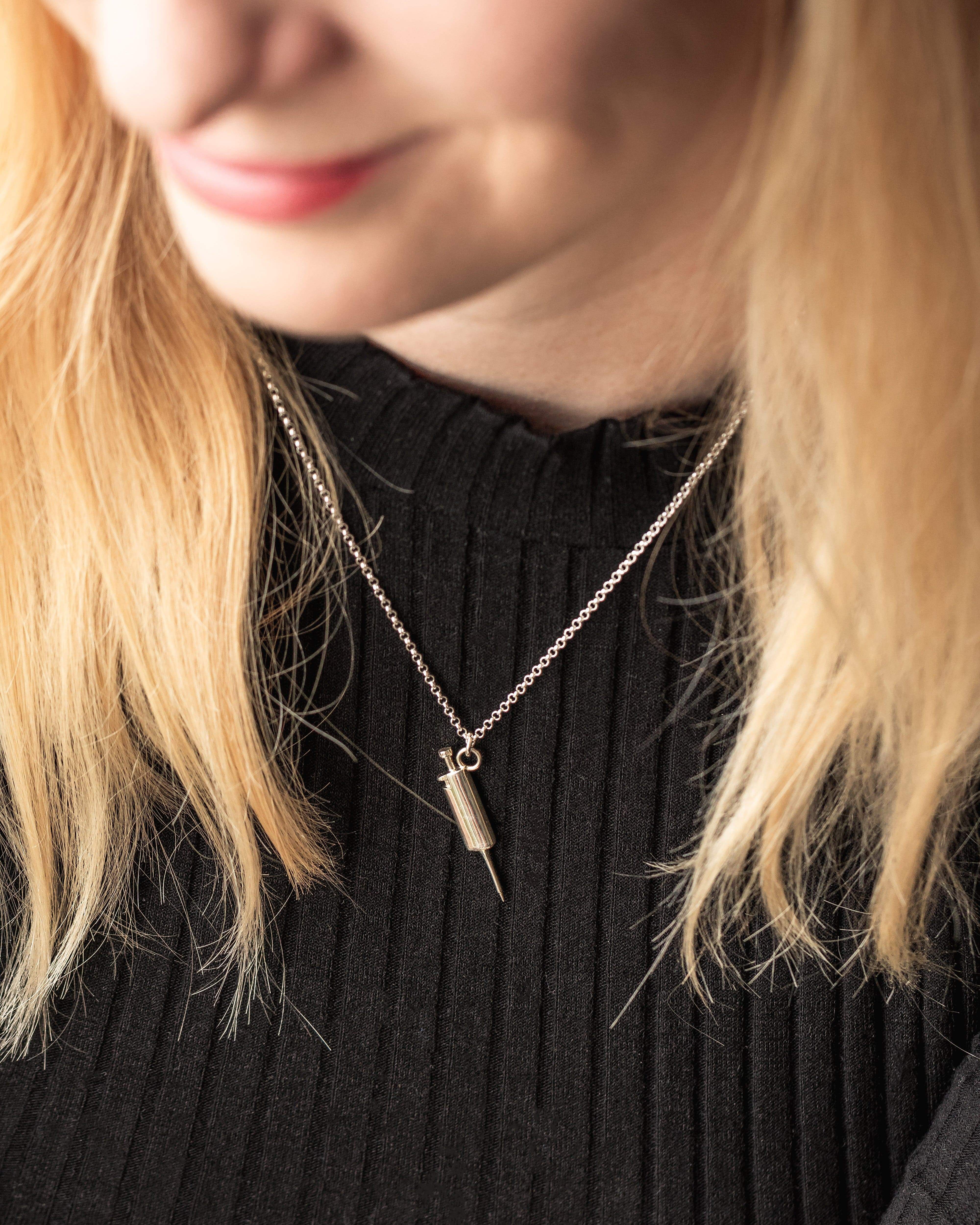 Close-up of a woman wearing the sterling silver pipette necklace, showcasing its stylish and precise design. Close-up of a woman wearing the sterling silver pipette necklace, showcasing its stylish and precise design.