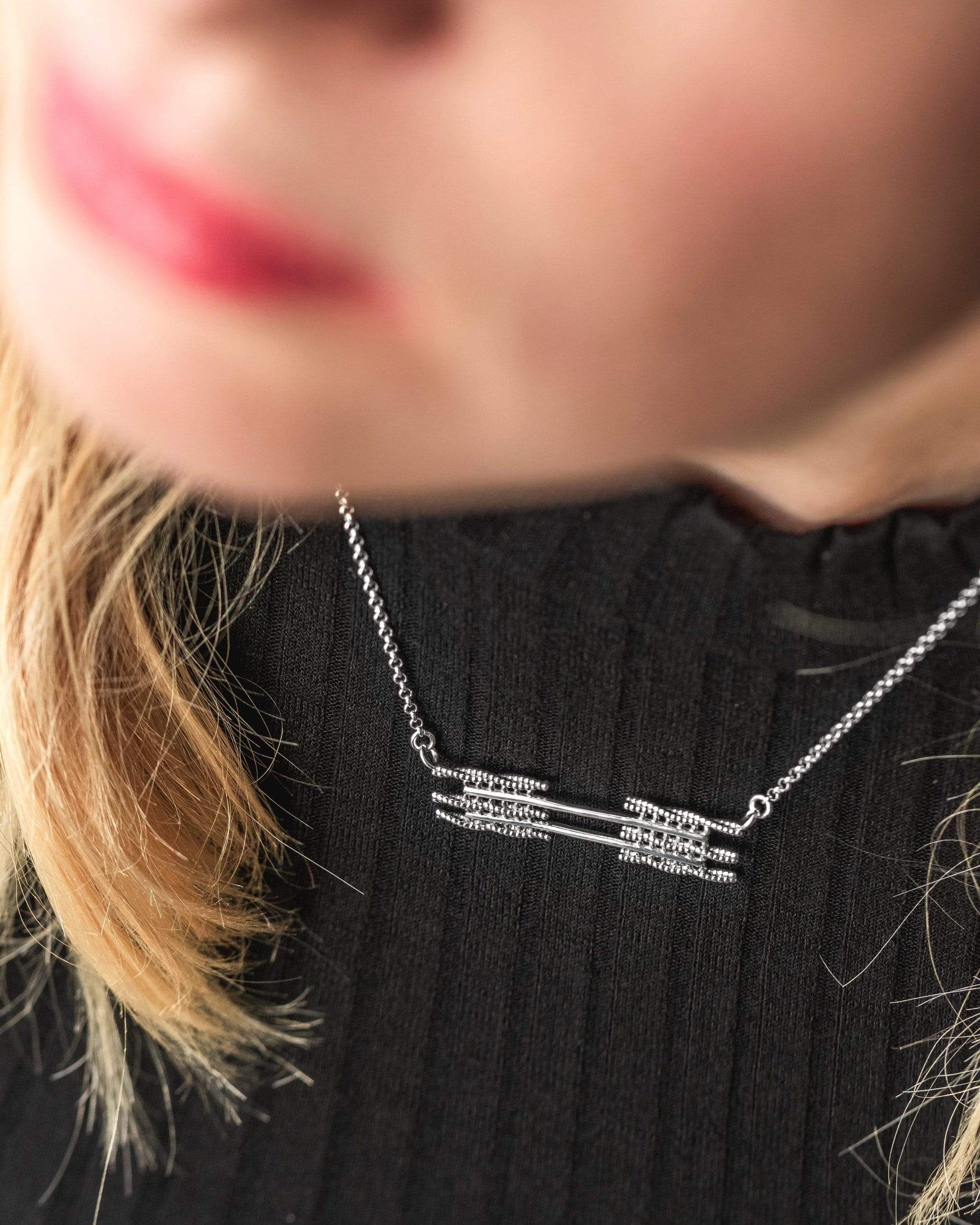 Close-up of a sarcomere necklace in silver, highlighting intricate muscle banding inspired detail. Close-up of a sarcomere necklace in silver, highlighting intricate muscle banding inspired detail.