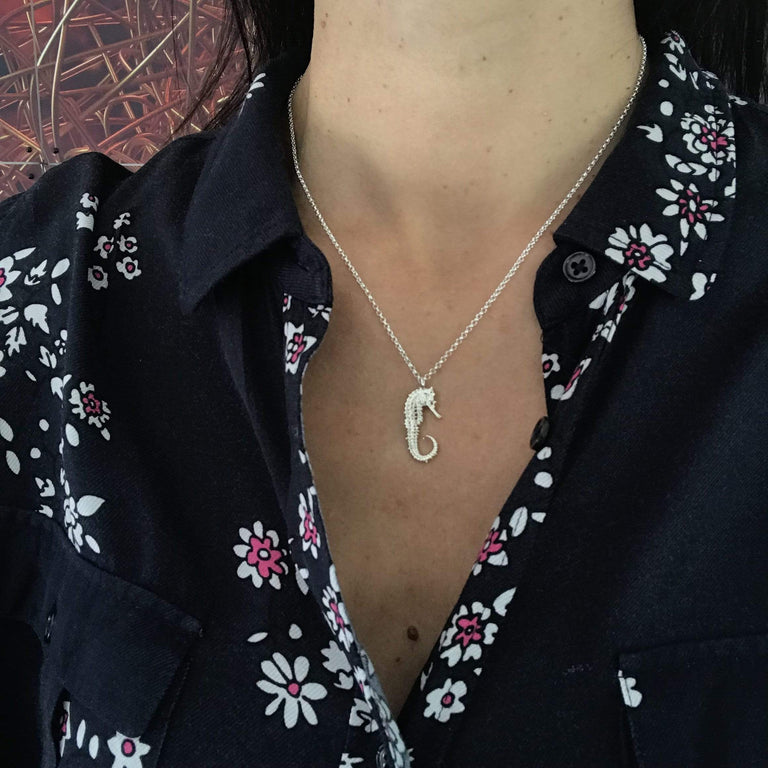 Woman wearing a delicate seahorse skeleton necklace in sterling silver, ocean-inspired and elegantly designed. Woman wearing a delicate seahorse skeleton necklace in sterling silver, ocean-inspired and elegantly designed.