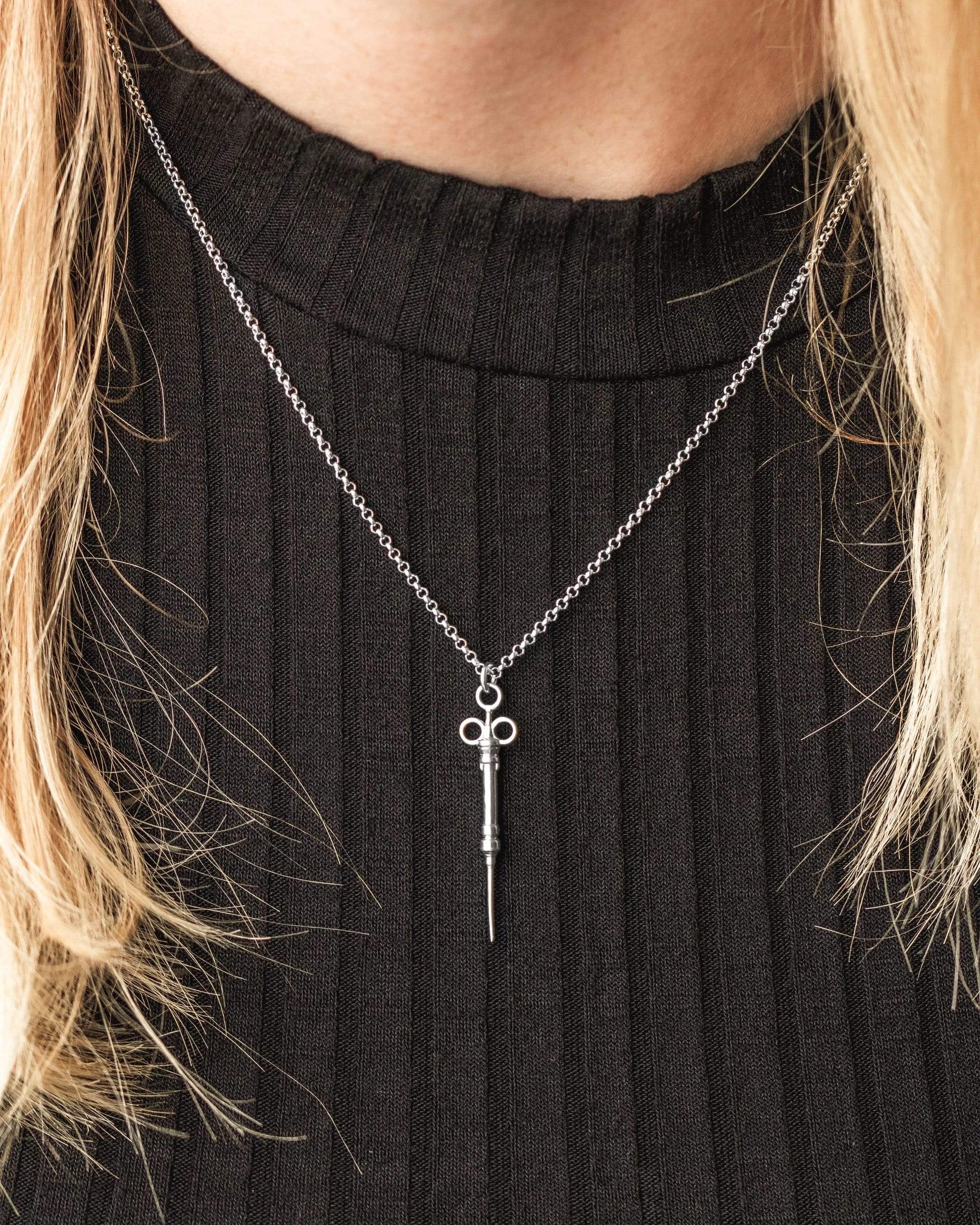 Close-up of a science-inspired syringe necklace, crafted in silver with intricate detailing. Close-up of a science-inspired syringe necklace, crafted in silver with intricate detailing.