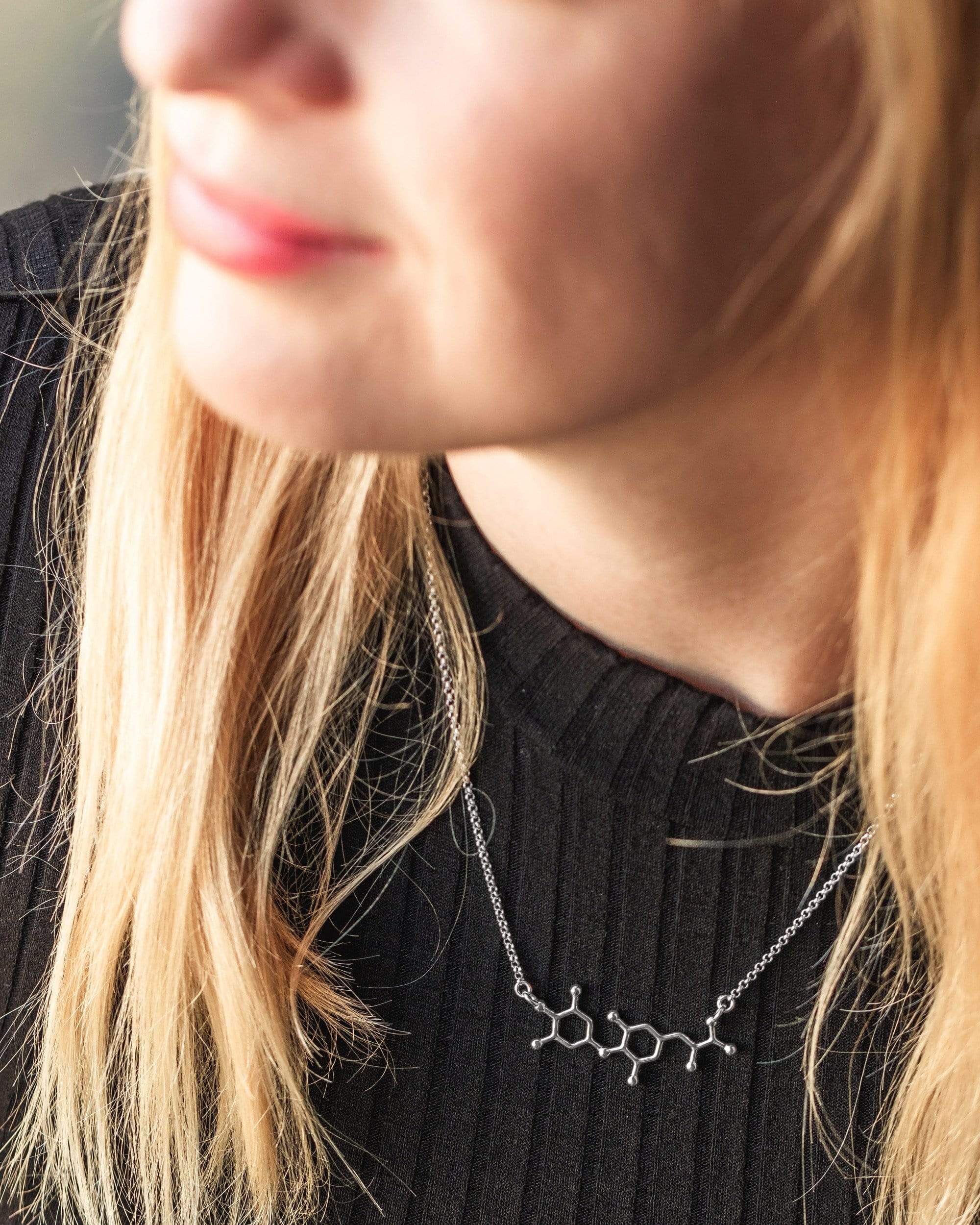 Woman wearing a silver T4 thyroid necklace, a stylish piece inspired by the science of metabolism. Woman wearing a silver T4 thyroid necklace, a stylish piece inspired by the science of metabolism.
