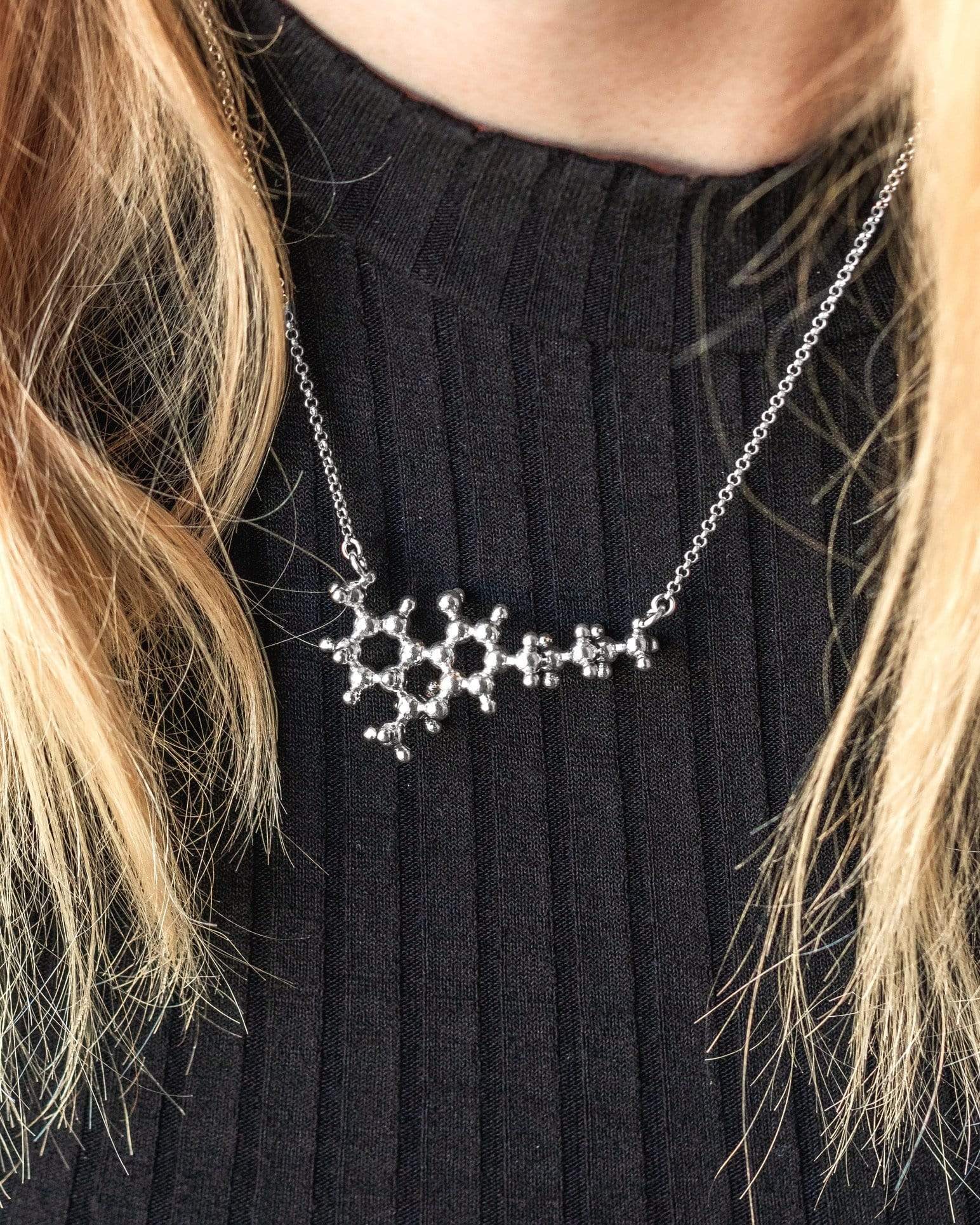 Close-up of the THC necklace on a model, highlighting its intricate molecular design in silver. Close-up of the THC necklace on a model, highlighting its intricate molecular design in silver.