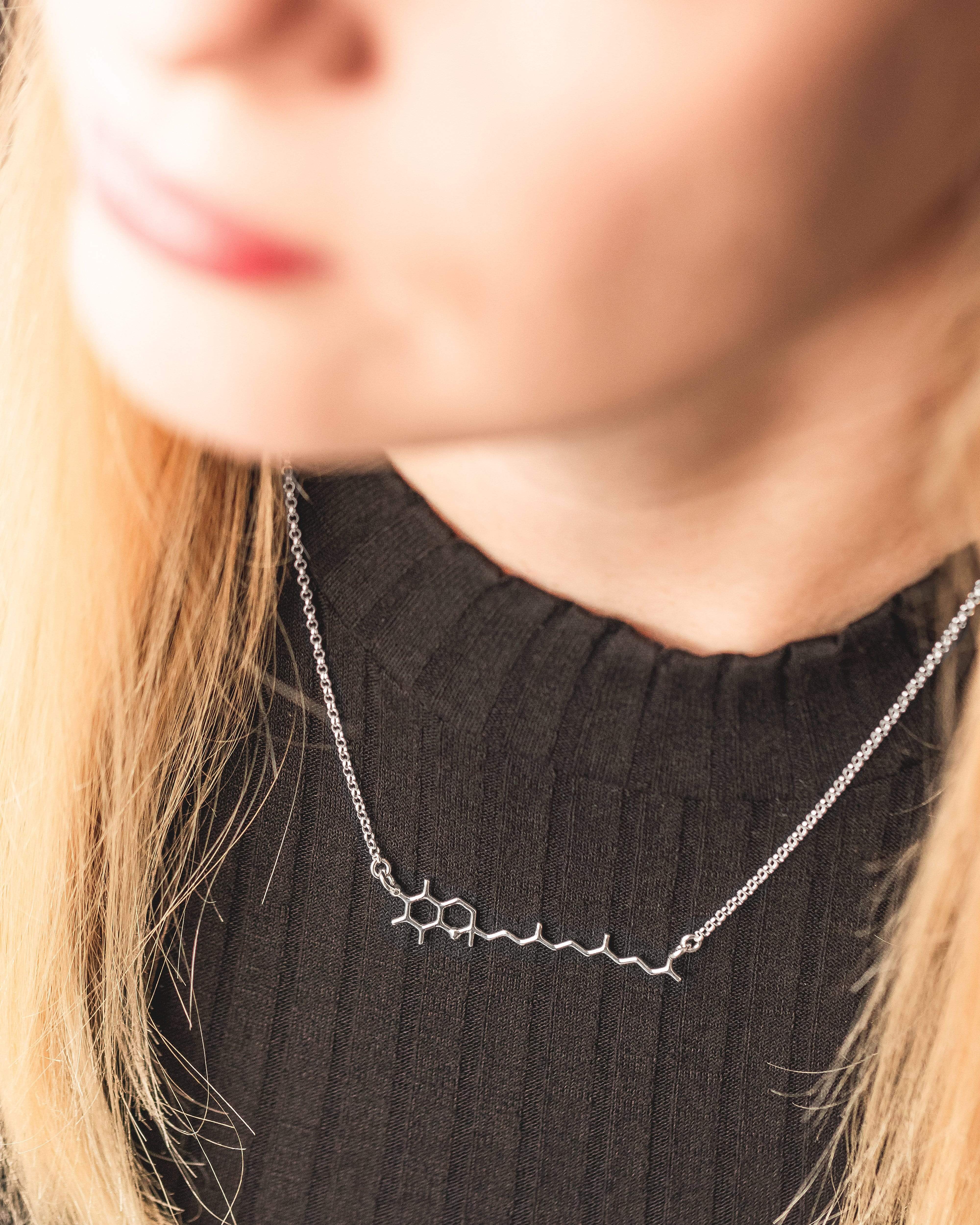 Close-up view of the Tocopherol Necklace worn on a model, highlighting its elegant and scientific design. Close-up view of the Tocopherol Necklace worn on a model, highlighting its elegant and scientific design.