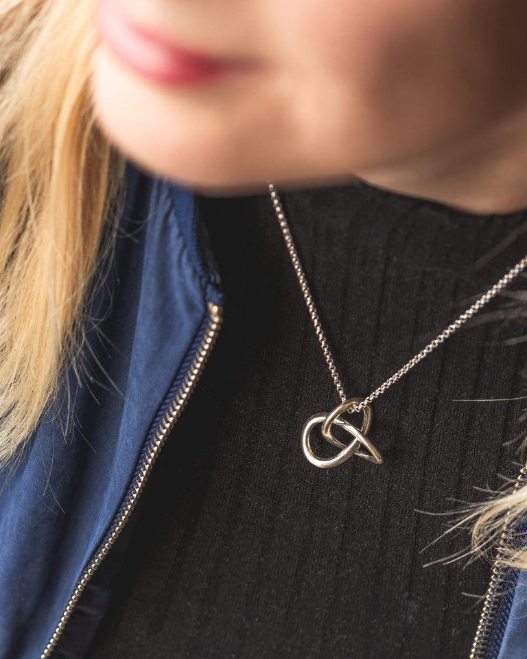 A model wearing the trefoil knot necklace in silver, showcasing its minimalistic and chic design. A model wearing the trefoil knot necklace in silver, showcasing its minimalistic and chic design.