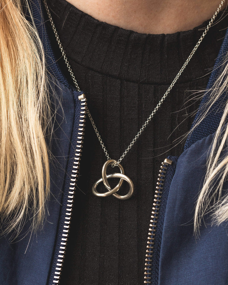 Silver trefoil knot necklace elegantly paired with a black outfit, perfect for science enthusiasts. Silver trefoil knot necklace elegantly paired with a black outfit, perfect for science enthusiasts.