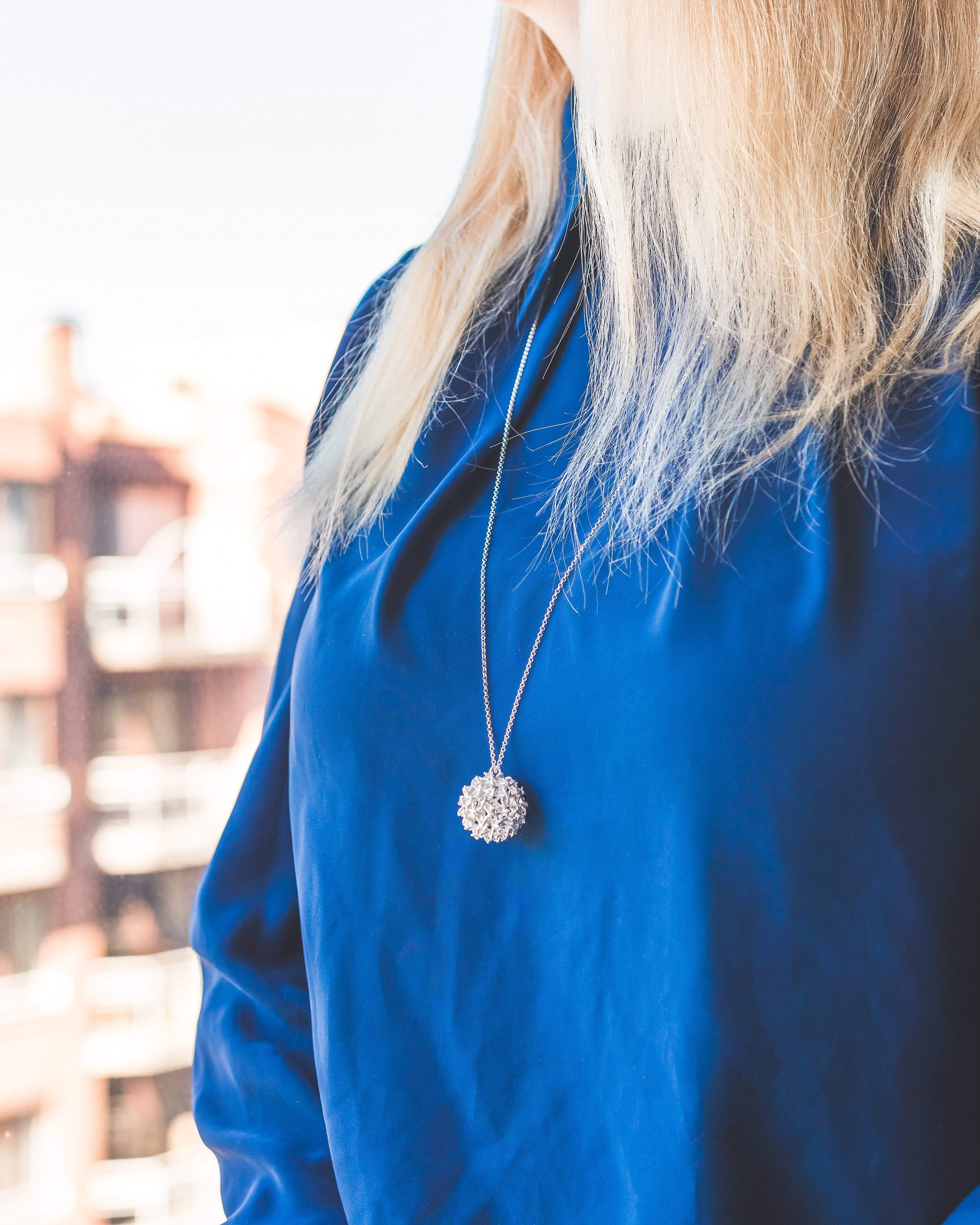 Woman wearing the West Nile Virus necklace, showcasing its elegant and unique scientific design. Woman wearing the West Nile Virus necklace, showcasing its elegant and unique scientific design.