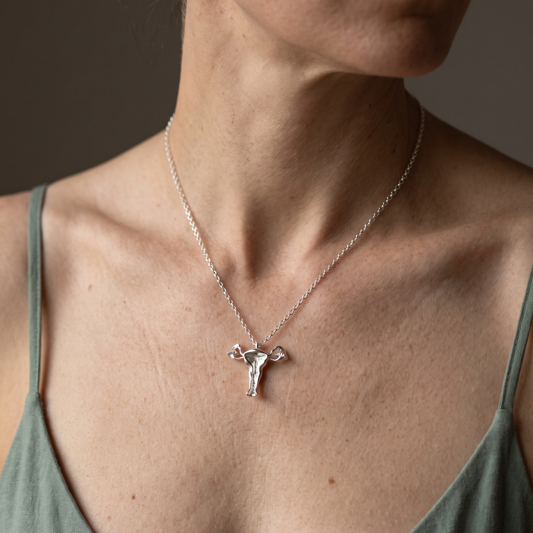 Woman wearing the sterling silver uterus necklace V on a fine silver chain, pendant resting below the collarbones