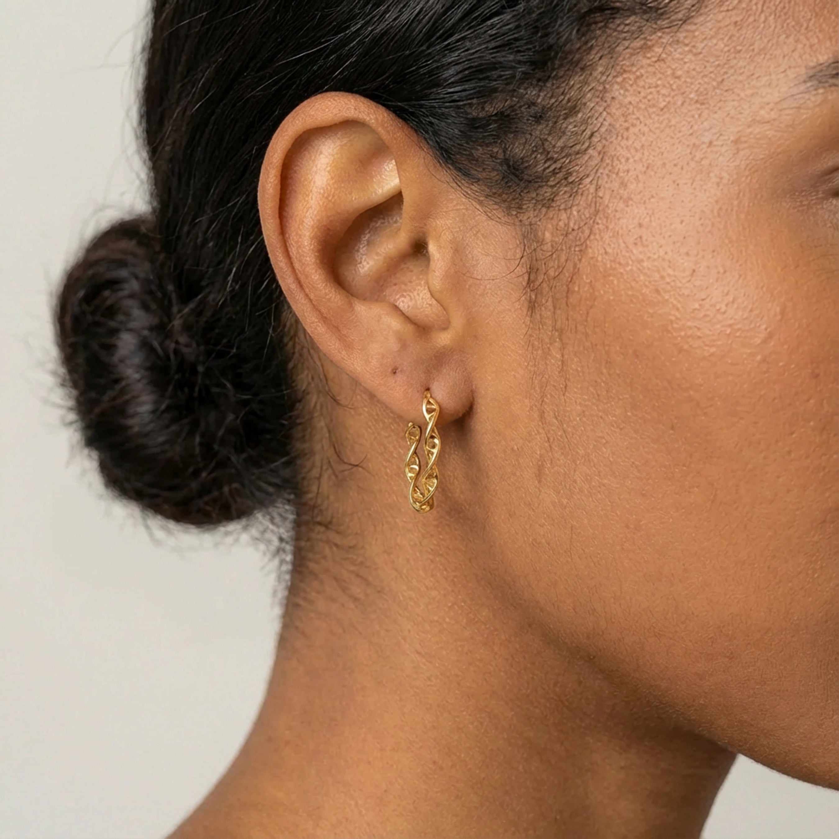 Woman wearing a small gold vermeil DNA hoop earring, close-up view of ear and hair tied back.