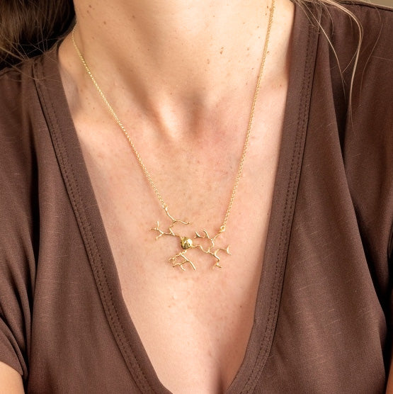 Close-up of a gold vermeil neuron necklace resting on the chest of a woman wearing a brown V-neck shirt.