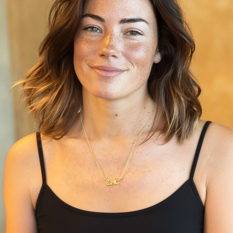 Woman wearing the gold vermeil E=MC² necklace, shown in a close-up portrait highlighting the pendant at her collarbone.