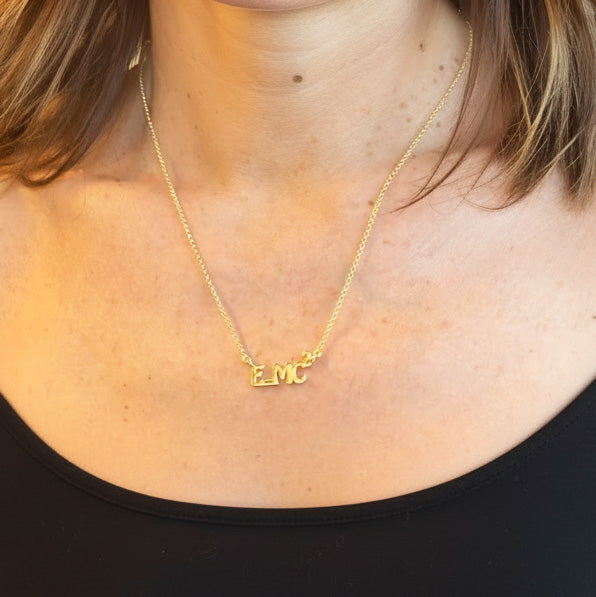 Close-up of the gold vermeil E=MC² necklace resting on a woman’s neck, showing the pendant’s size and shine in natural light.