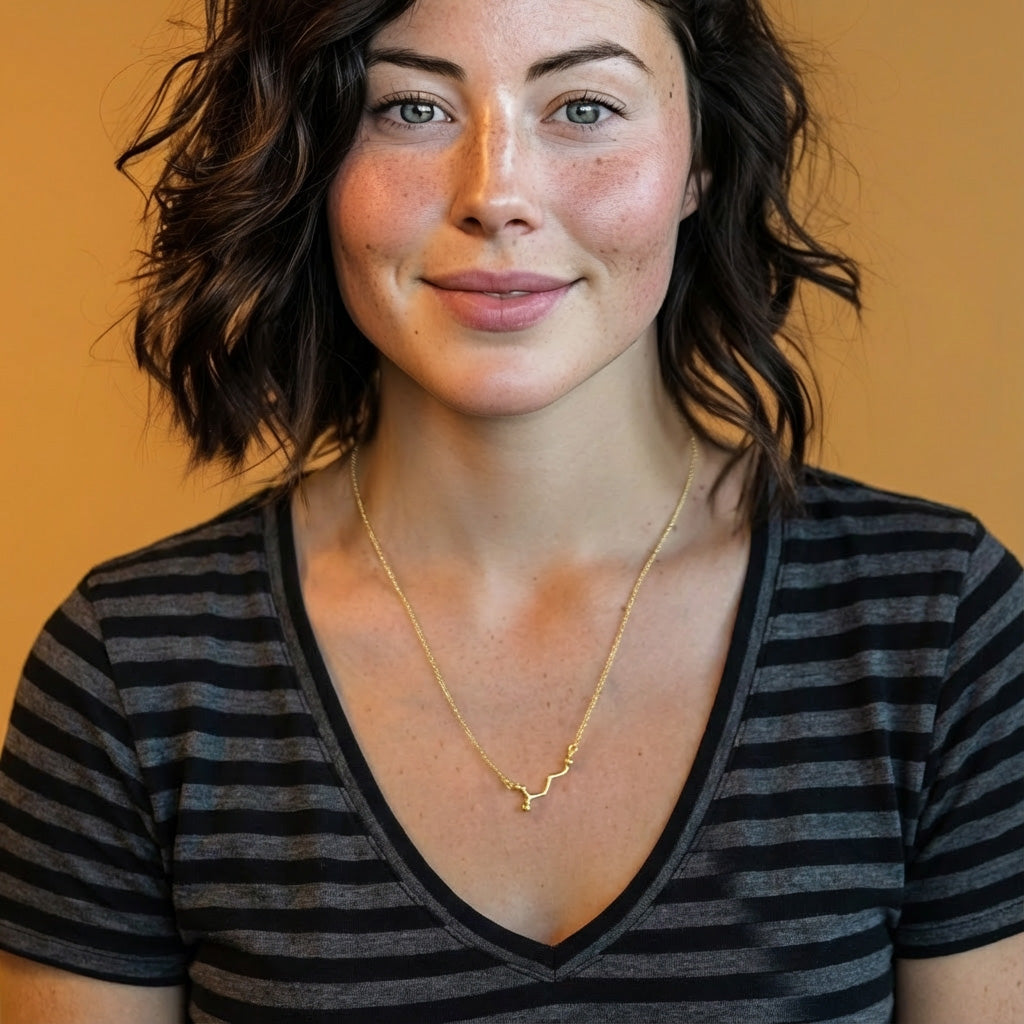 Woman wearing the gold vermeil GABA necklace layered with another chain, smiling and facing the camera in a striped V-neck shirt.