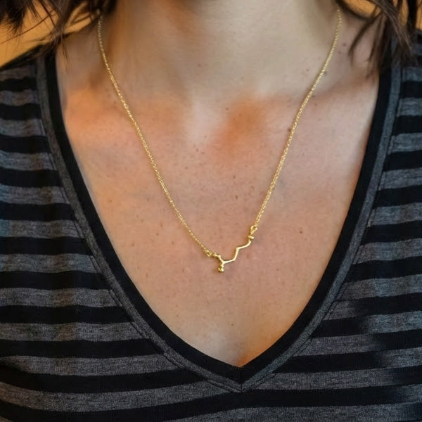 Close-up of the gold vermeil GABA pendant resting on the model’s chest, showing the fine details of the molecular structure and the delicate chain.