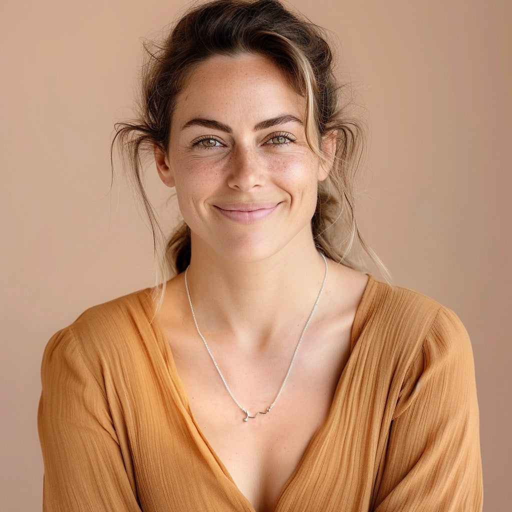 Smiling woman wearing the GABA necklace over a warm brown blouse, showcasing the elegant and minimal molecular design.