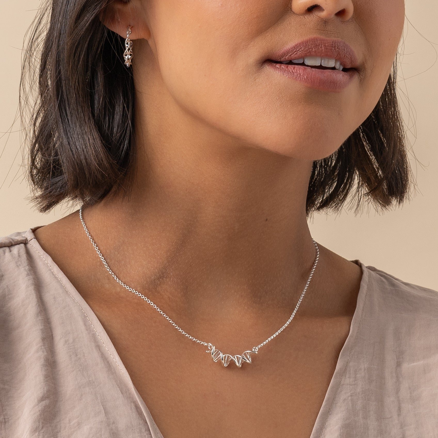 Close-up of a model wearing a silver DNA necklace, highlighting the delicate double helix design against her skin.