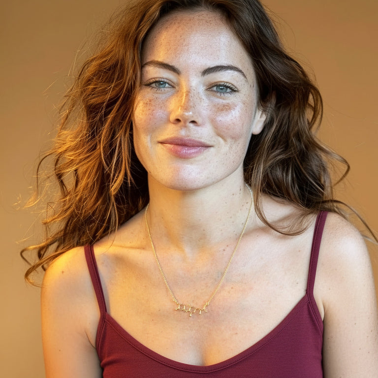 Portrait of a woman wearing a gold vermeil T3 thyroid hormone necklace, looking slightly off-camera, with warm studio lighting highlighting her face and the pendant.