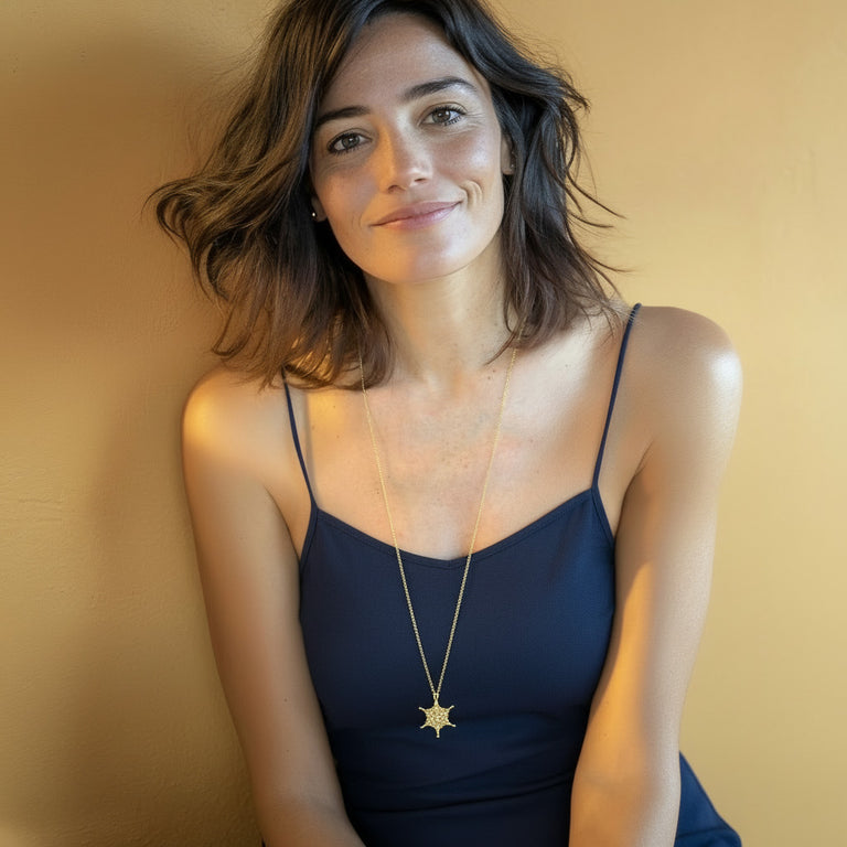 Woman wearing a navy top and a gold vermeil adenovirus pendant necklace, shown from the waist up while sitting and smiling at the camera.