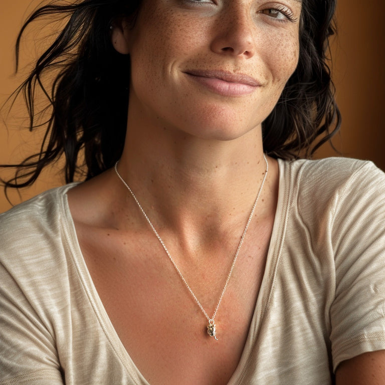 A smiling woman wearing the appendix necklace in silver, styled casually with a beige t-shirt, showcasing the necklace’s size and fit.