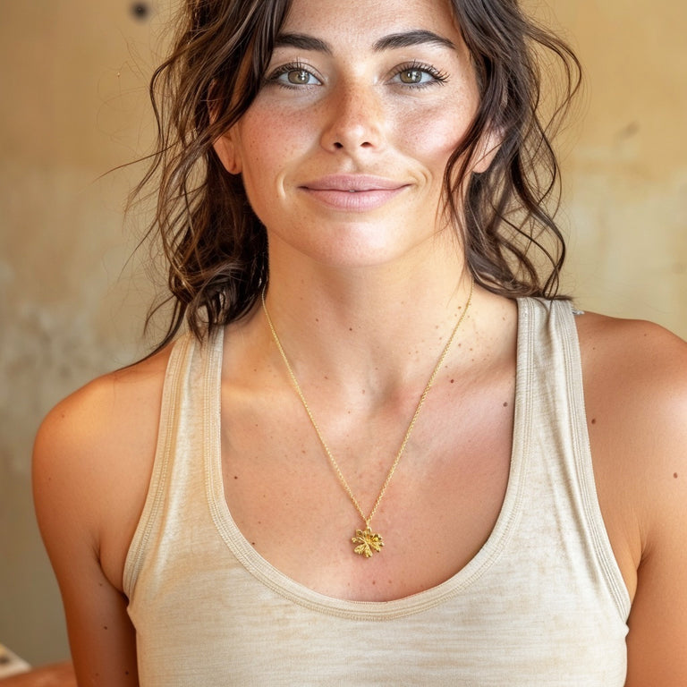 A smiling woman with wavy dark hair wearing a beige tank top and the Arabidopsis necklace, showing how the pendant looks when worn.