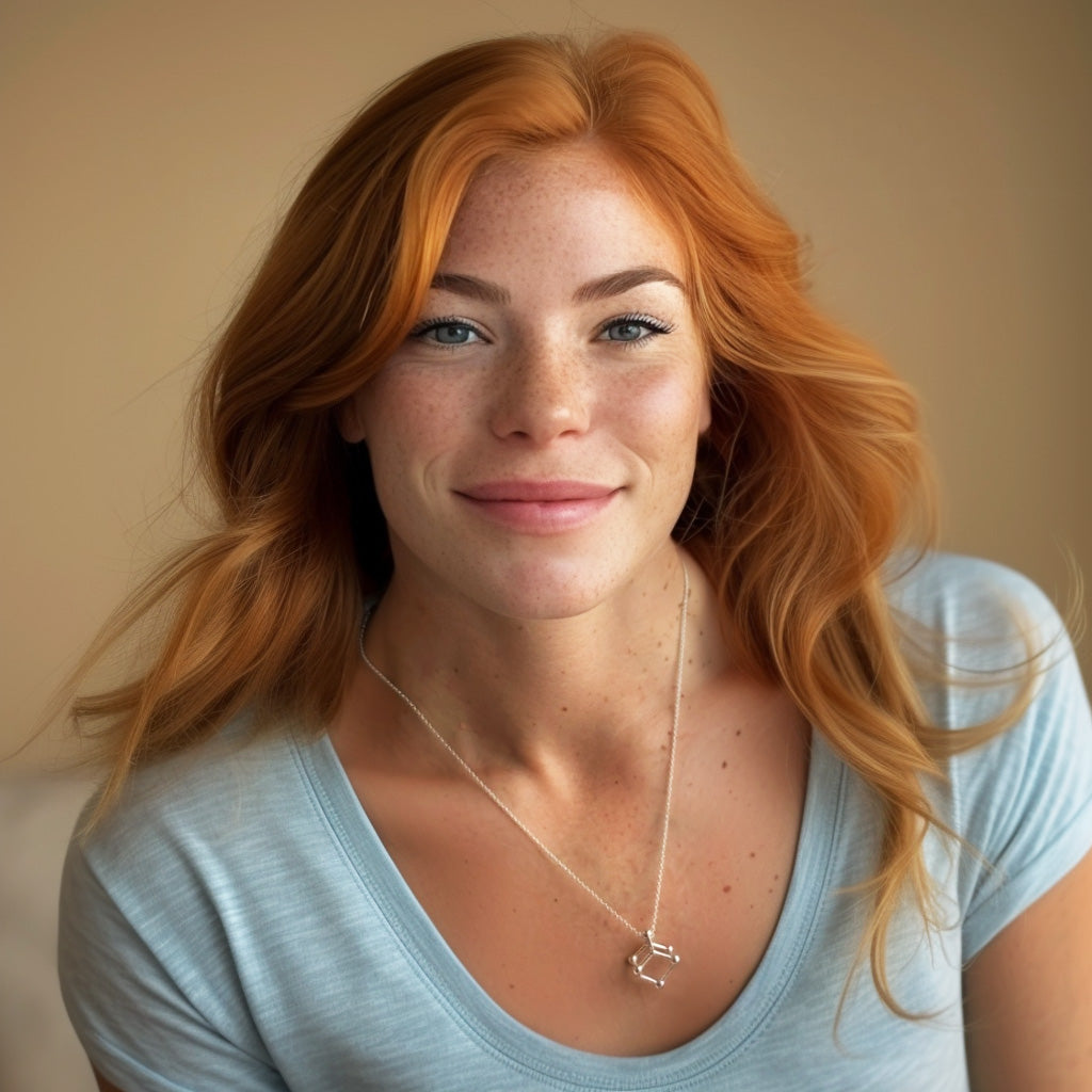 Smiling woman with long red hair wearing a light blue shirt and the arsenic trioxide molecular structure necklace, looking directly at the camera.